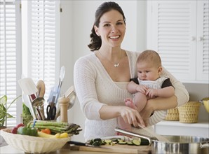 Mother holding baby and cooking.