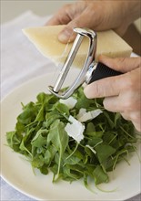 Man shaving cheese onto salad.