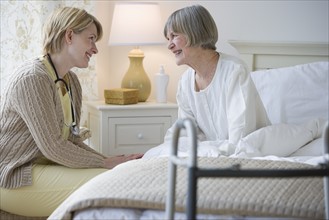 Nurse talking to senior woman in bed.