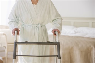 Senior woman using walker in bedroom.