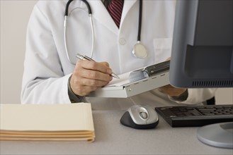 Doctor writing on chart at desk.