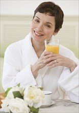 Woman wearing bathrobe and drinking juice.
