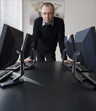 Businessman leaning on table with computers.
