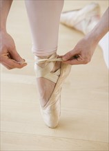 Female ballet dancer tying pointe shoes.