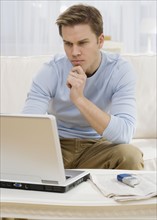 Man looking at laptop on sofa.
