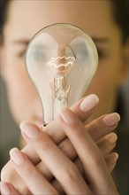 Woman holding light bulb in front of face.