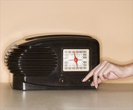 Woman turning knob on old fashioned radio.