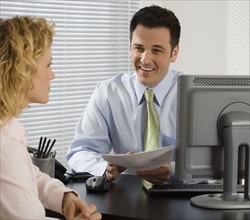 Businessman consulting with businesswoman at desk.