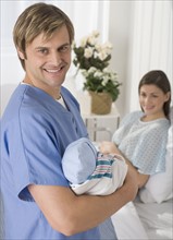 Portrait of father holding newborn baby in hospital.