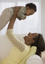 Mother playing with baby on sofa.