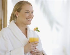 Woman wearing bathrobe and drinking cocktail.