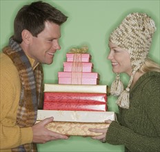 Couple holding stack of Christmas gifts.
