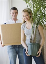 Couple holding moving box and plant.