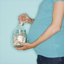 Pregnant woman putting money in jar.