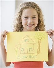Girl holding up drawing of new house.