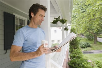 Man reading newspaper on porch.