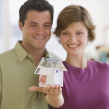 Couple holding model house made of Euro banknotes.