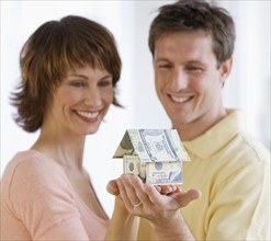 Couple holding house made of money.