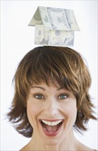 Woman with house made of money on head.