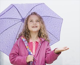 Girl standing under umbrella with hand out.