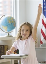 Girl raising hand at school desk.