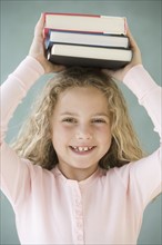 Girl holding stack of books on head.