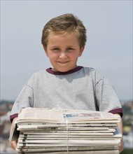 Boy holding stack of bundled newspapers.