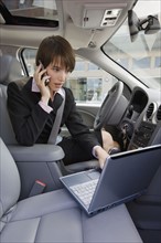 Businesswoman typing on laptop in car.