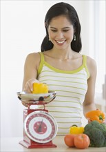 Woman weighing vegetables in kitchen.