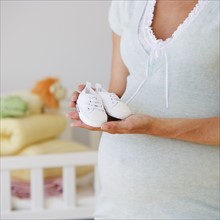 Pregnant woman holding baby shoes.