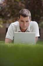 Man using laptop in grass.