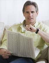 Man holding newspaper on sofa.