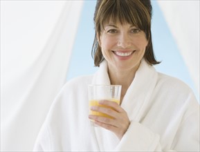 Woman in bathrobe holding juice.