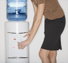 Businesswoman filling cup at water cooler.