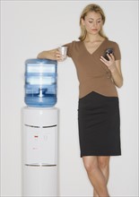 Businesswoman looking at cell phone next to water cooler.