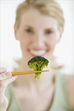 Woman holding broccoli in chopsticks.