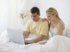 Couple looking at laptop in bed.