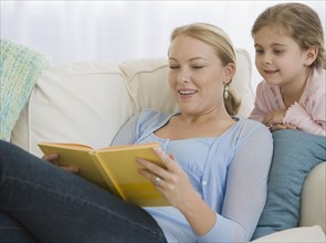 Mother reading to daughter on sofa.
