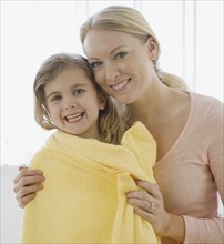 Mother hugging daughter wrapped in towel.