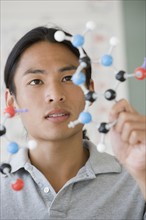 Asian male college student looking at molecule model.