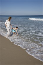 Mother and daughter standing in ocean surf.