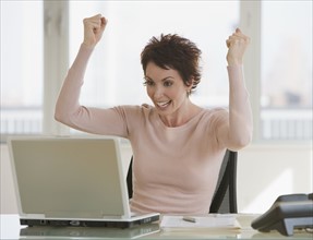 Businesswoman cheering at laptop.