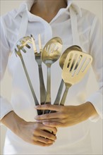 Woman holding assorted serving utensils.