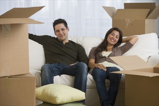 Multi-ethnic couple surrounded by moving boxes.