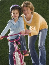 Mother helping daughter ride bicycle.
