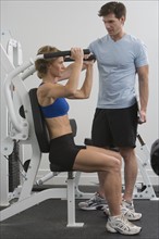 Personal trainer assisting woman on exercise machine.
