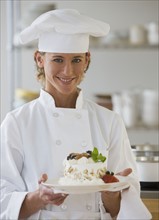 Female chef holding plate of dessert.