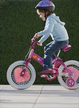 Girl riding bicycle with training wheels.