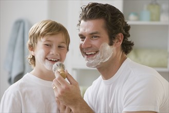 Father putting shaving cream on son’s face.