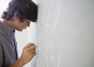 Teenaged boy writing math equations on blackboard.
